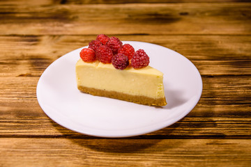 White plate with cheesecake New York and raspberries on wooden table