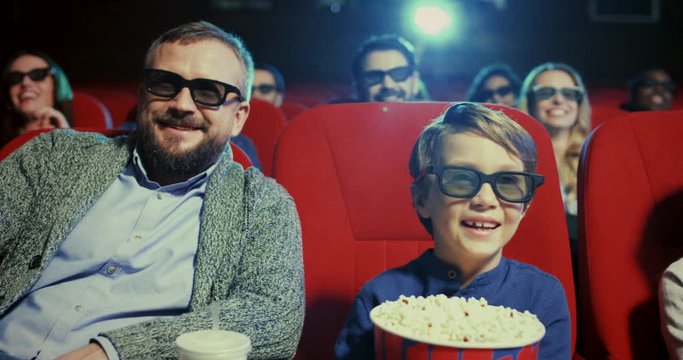 Caucasain cite smiled kids, sister and brother, in 3D glasseswith their father and popcorn and laughing while watching comedy film in the cinema.