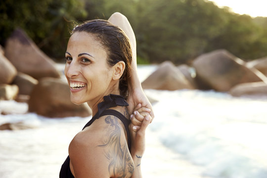 Seychelles, portrait of smiling woman with tatoo doing yoga exercise on the beach