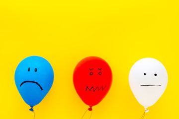 Negative emotions concept. Balloons with drawn faces on yellow background top view space for text