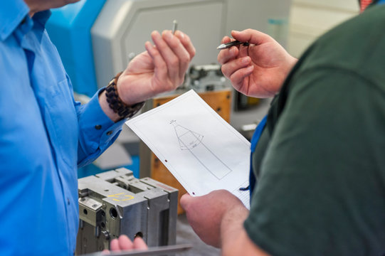 Two men discussing a metal workpiece