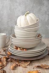 A stack of plates of different sizes on the table decorated with white pumpkin autumn leaves and nuts . autumn