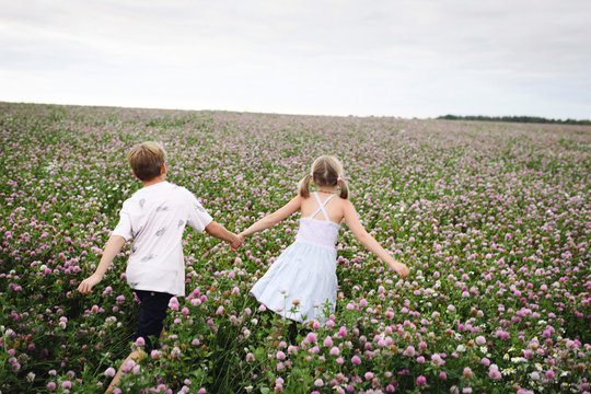 Two smiling children running over clover field