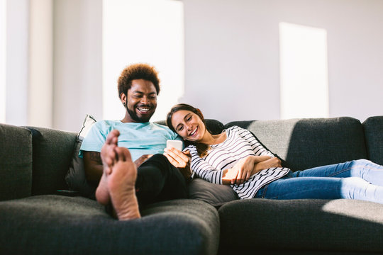 Young couple lying on couch looking at smart phone