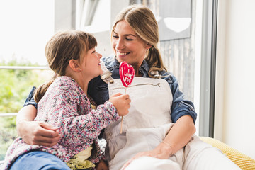 Happy mother and daughter with lollipop at the window at home