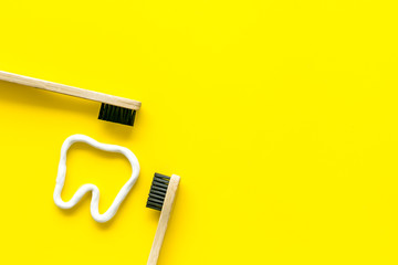 Teeth brushing concept. Tooth drawn with toothpaste near toothbrushes on yellow background top view space for text