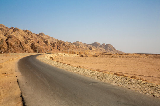 Empty road by rock formation in desert against clear blue sky