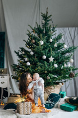 Attractive happy mother in retro orange dress with her little cute son on christmas decoration background