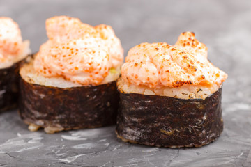Japanese maki sushi rolls with flying fish roe, cheese on black concrete background. Side view.