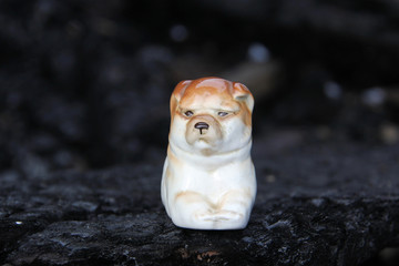 Ancient ceramic statuette of a lying dog on the ruins of a burned wooden house