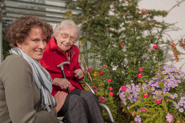 Obraz premium Smiling senior woman with wheelchair and young woman in the garden