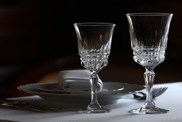 Served cutlery sets, plates, napkins, empty crystal wine glasses, on tables in a restaurant.
