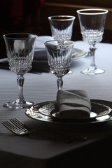 Served cutlery sets, plates, napkins, empty crystal wine glasses, on tables in a restaurant.