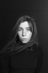 Black and white portrait of a beautiful girl with hair flying in the wind on a dark background