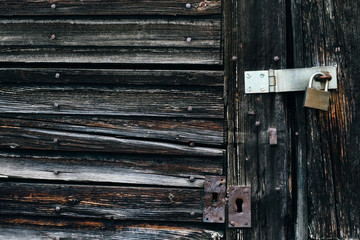 Close up detail of ancient weathered brown wooden door locked shut with metal hinge and padlock