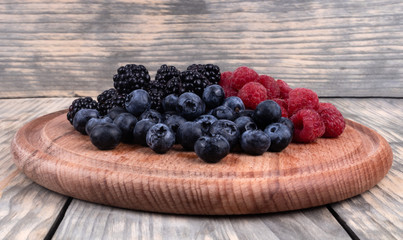 Side view of a pile of ripe red, blue and black berries laying in wooden plate
