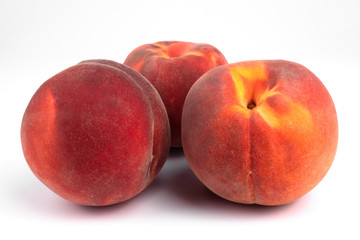 Three red orange freshly collected peaches laying next to each other on white background