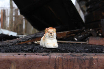 Ancient ceramic statuette of a lying dog on the ruins of a burned wooden