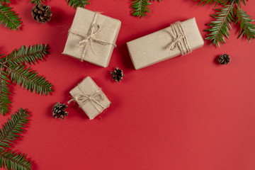 Christmas or winter composition. Frame made of fir tree branches, pine and handmade gift boxes on pastel red background. Christmas, winter, new year concept. Flat lay, top view, copy space