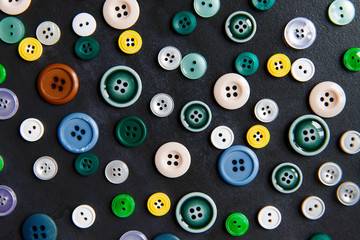 Colorful mixed sewing buttons on black background, flat lay. Top view.