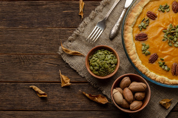 homemade pumpkin pie , pumpkin seeds and autumn leaves on a wooden background