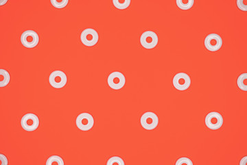 Flat round white plastic beads in regular pattern on red cardboard background