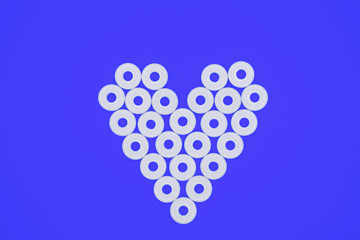 Heart pattern made of white flat round plastic beads laying on blue cardboard background