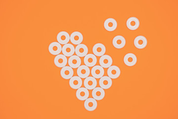 Heart pattern made of white flat round plastic beads laying on orange cardboard background