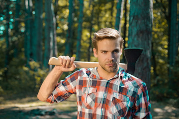 Obraz premium Lumberjack on serious face carries axe on shoulder. Bearded man with axe concept. Lumberjack with axe on forest background. Man doing mans job. Harvest of timber.