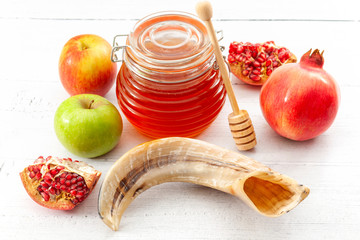 Happy Rosh Hashanah, judaism, traditional autumn holiday in jewish culture and judaic new year conceptual idea with ram horn or shofar, jar of honey, apple and pomegranate isolated on wood background