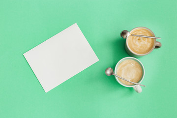 Two cup coffee cappuccino, small spoon and blank paper for writing ideas. Time for rest and reflection. Top view and flat lay with trend color mint background.
