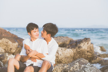 Homosexual portrait young asian couple sitting hug together on rock or stone in the beach in summer, asia gay going tourism for leisure and relax with happy in vacation at sea, LGBT legal concept.