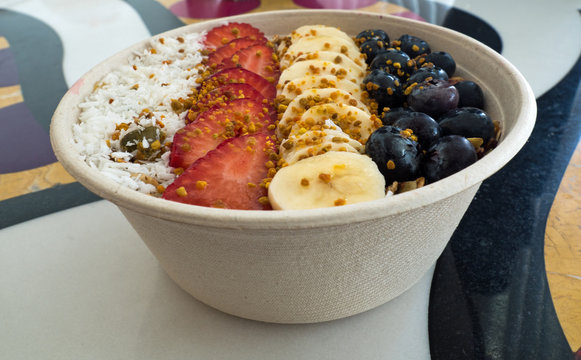 Acai bowl super food, shaved coconut, sliced strawberries, bananas and blue berries covered with bee pollen and honey