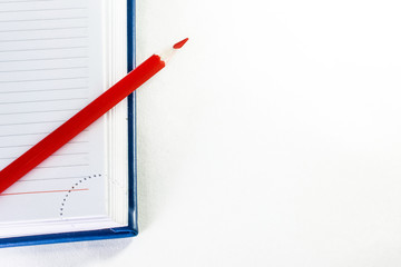 red pencil on a blue Notepad open in the right corner of the frame on a white background