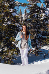 Portrait of a young beautiful brunette woman with blue eyes and freckles on face in winter snowy mountain landscape. Beautiful girl in the winter outdoors.