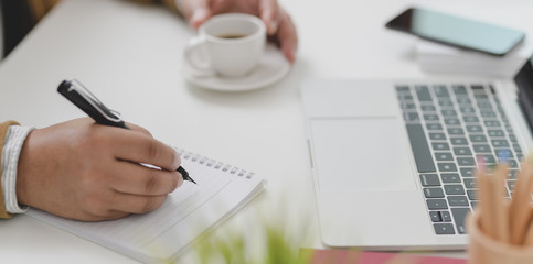 Businessman working on his project while writing the idea on notebook and drinking a cup of coffee