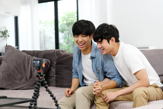 Two young asian men friend taking photo together, asia gay couple selfie with phone while sitting in home living room, friendship, homosexual and lgbt concept