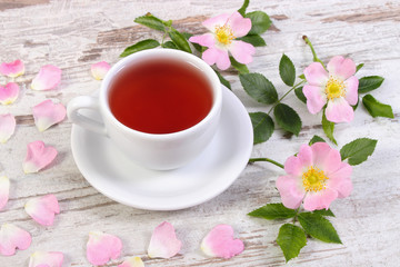 Cup of tea and wild rose flower on old rustic board