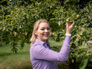 Fröhlich lächelnde junge Frau steht unter einen Apfelbaum