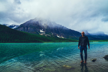 Fototapeta na wymiar Fashionable Man Standing On Beautiful Mountain Lake Shore Outdoor Adventure Woodsman