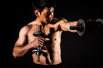 Naklejka na ściany i meble sport man standing doing exercise for arms with dumbbells and showing muscle bodybuilding on black backgrounds, fitness concept, sport concept