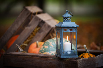 Grey lantern with burning candle on wooden box decorated in autumnal style,   in rustic style....