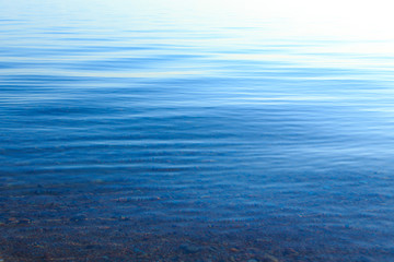 Naklejka premium Clear water texture in blue and orange. Background of the ocean and the sea backlit by the sun. Soft waves. Natural water