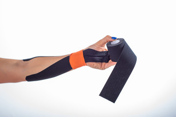 Physiotherapy for a diseased wrist. Alternative medicine. Adhesive tape for athletes with injuries. Support for an injured arm. Female hand on a white background holds a roll of kinesiotape.