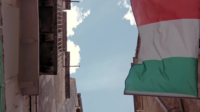Italian flag waving on a balcony against the sky and the rooftops in a typical narrow Italian street. Slow motion shot.