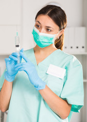 Female nurse in mask holding syringe for injection in hospital