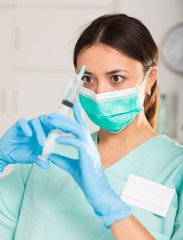 Female nurse in mask holding syringe for injection in hospital