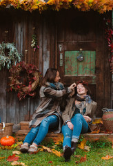 two beautiful young women, covering their faces with a yellow autumn leaf, smiling on an old wooden background.