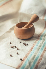 rustic flat lay, wooden mortar with wooden pestle for grinding spices on linen background and with peppercorns on windowsill