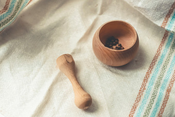 rustic flat lay, wooden mortar with wooden pestle for grinding spices on linen background and with peppercorns on windowsill